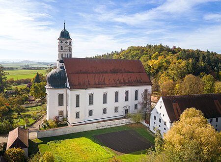 Eine große Kirche aus der Luft. Darum herum andere Gebäude, grüne Wiese und ein Hügel mit grünen Bäumen.